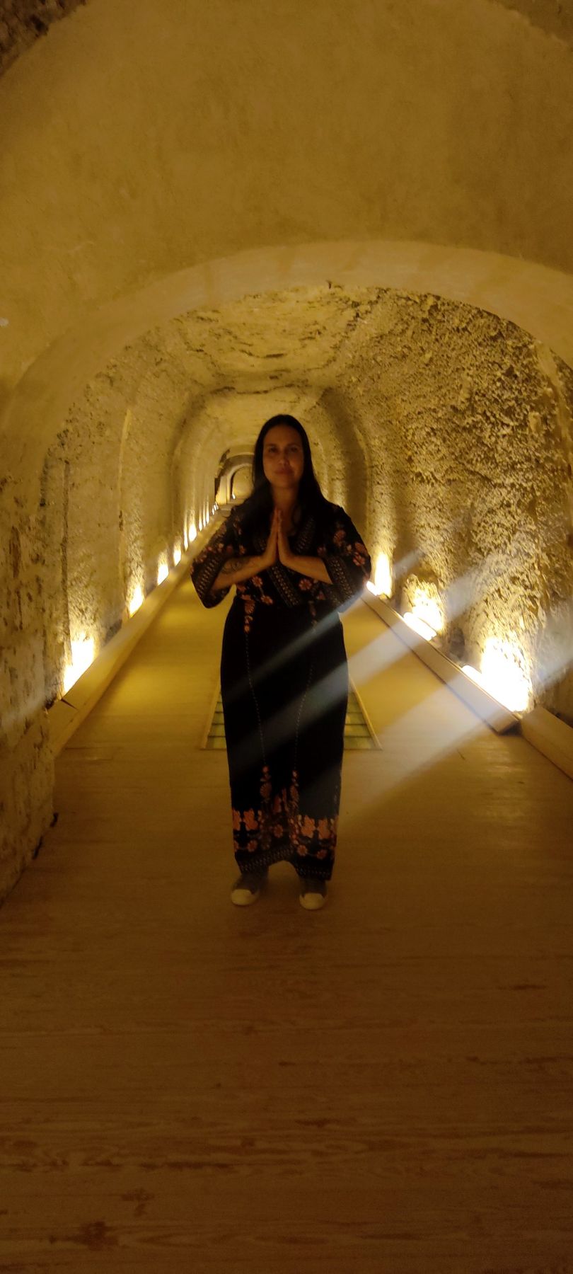 Letícia Bhakti em um túnel iluminado, com as mãos em prece